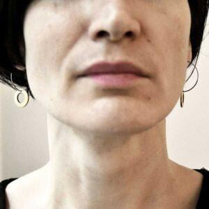 Zdjęcie pokazuje widoczną z przodu twarz kobiecą a na uszach nasze autorskie kolczyki koła NAGANO 19 ze stali chirurgicznej i mosiądzu a te kolczyki wyglądają wprost obłędnie