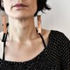 Biżuteria Na zdjęciu kobieta patrzy w obiektyw a na uszach ma piękne w swojej prostocie i elegancji nasze oryginalne autorskie kolczyki z długich pasów miedzi zawieszonych swobodnie na dużych biglach ze stali chirurgicznej.