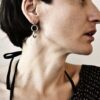 Kobieta na zdjęciu patrzy w bok i widząc jej profil można podziwiać w jej uchu zachwycający kolczyk wykonany z trzech okręgów w cudownych proporcjach