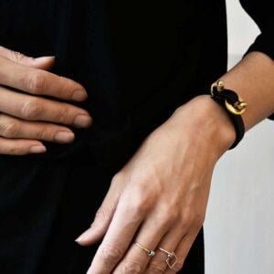 Minimalistyczna czarna bransoletka FUKUI24 na tym zdjęciu wykonana jest z mosiądzu w naturalnym kolorze oraz super kauczuku w kolorze czarnym i zachwyca na kobiecym nadgarstku ale to wzór biżuterii unisex i wygląda obłędnie również noszony przez mężczyzn jaka biżuteria na wiosnę modna modne bransoletki prezent