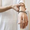 Zdjęcie pokazuje kobiece ręce a na jednym nadgarstku widać tą współczesną i oryginalną bransoletkę w srebrnym kolorze wykonaną ze stali chirurgicznej z dużym intrygującym zapięciem, to srebrna bransoletka 'NAGANO'24