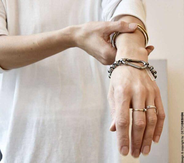 Zdjęcie pokazuje kobiece ręce a na jednym nadgarstku widać tą współczesną i oryginalną bransoletkę w srebrnym kolorze wykonaną ze stali chirurgicznej z dużym intrygującym zapięciem, to srebrna bransoletka 'NAGANO'24