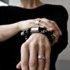 Na tym zdjęciu na kobiecym nadgarstku widać z przodu w dużym skrócie obłędną bransoletkę unisex wykonaną z czarnej liny oraz tulei i zakończeń ze stali chirurgicznej
