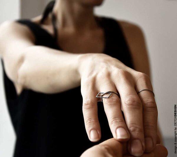 Srebrny pierścionek NAGANO 25 widoczny na kobiecej dłoni obłędnie wygląda na palcu zdobiąc niezwykle dłoń a przemieszczający się po nim swobodnie kwadrat zachwyca proporcjami i czyni ten model pierścionka niezwykle lekkim.