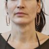 Oryginalne kolczyki Nagano80 z miedzi w kształcie dużych spinaczy wiszące przy twarzy projektantki DETOXDESIGN.
